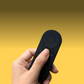Lightweight remote control for Pivo Pods, held in hand, against yellow background.